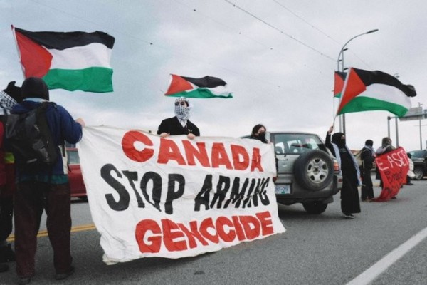 Activists with flags form a cordon, holding a banner reading CANADA STOP ARMING GENOCIDE