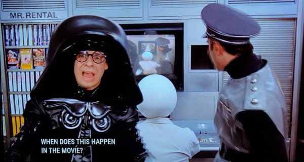 Scene from Spaceballs the Movie™️
We see Dark Helmet & Colonel Sanderz standing in front of a video wall and a lineup of VHS tapes. There's a sign above the tapes reading "Mr. Rental." An officer w/a round white helmet sits with his back to us and on the screen in front of him is an exact replication of what we the viewer are looking at. Dark Helmet is looking at the camera with a perplexed, terrified, confused look on his face. His mask is up and you can see his face, kind of a nerdy looking fellow with big round glasses wearing a giant domed black helmet and black uniform, similar to Darth Vader but not as menacing. Picture 1, closed caption reads, "When does this happen in the movie?" Picture 2, with Colonel Sanderz now speaking, closed caption reads,"Now. You're looking at now, sir." Picture 3, Colonel Sanderz continues while Dark Helmet continues to look absolutely befuddled, "Everything that happens now is happening now."