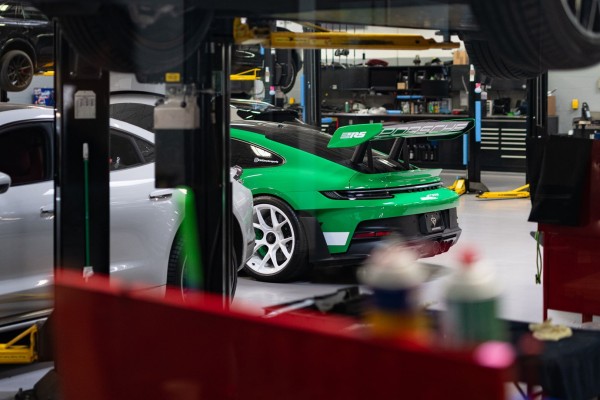 The tail end of a green sports coupe with a big wing, seen in an automotive repair bay.
