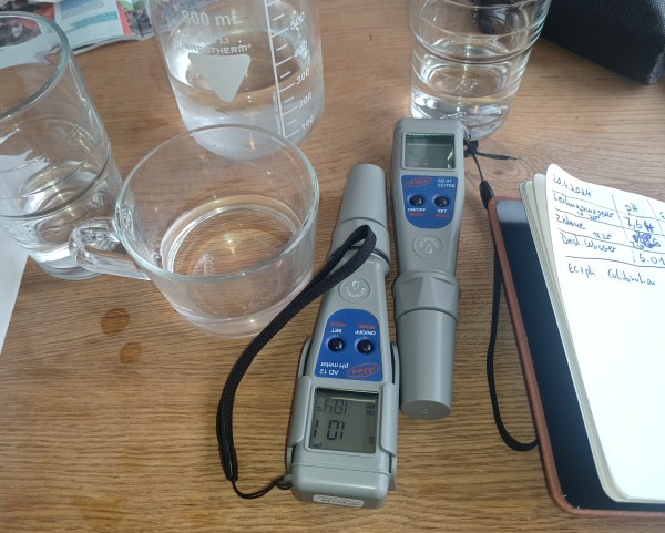 Gläser und Becherglas mit Wasser sowie ein EC- und ein pH- Messgerät sowie Notizbuch