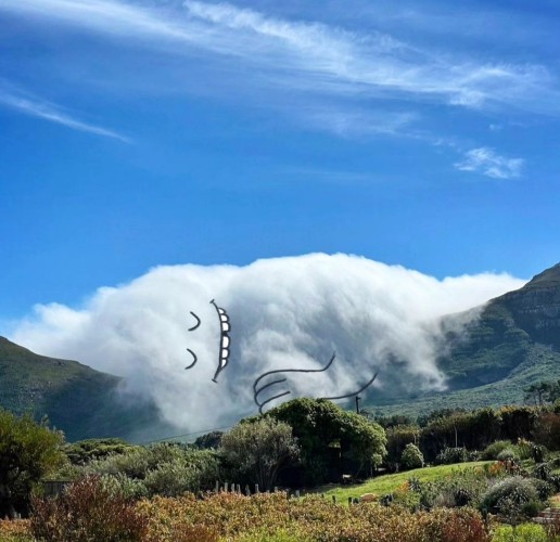 Photography. A color film shot of a white cloud against a blue sky, above a green valley. Between two hills is a broad white cloud that has settled mistily over a landscape of trees and meadows. The artist has embellished the cloud with a felt-tip pen. Two U-shaped arches as eyes, an open smiling mouth with a gap between the teeth and an arm. Now a sleeping, grinning cloud lies in its green bed and dreams peacefully of the rising sun.
Info: ChrisJudge aka "ADailyCloud" (Instagram) takes cloud photos from the Internet and paints faces on them. This is how he transforms the countless cloud pictures into a unique image that makes us smile.