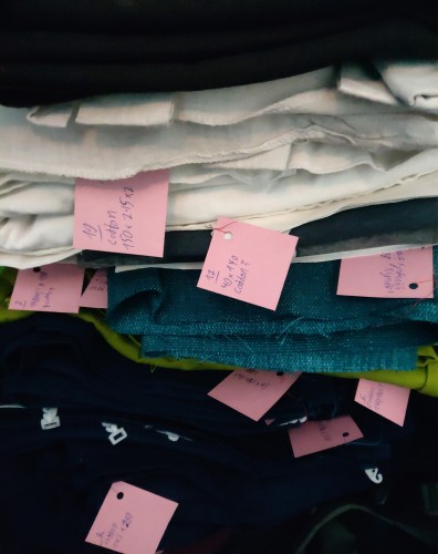 Stack of different fabrics with small tags attached to each. they each have a number, the material and measurements written on them.