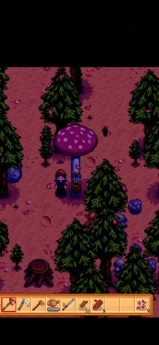 A screenshot from Stardew Valley, showing my farmer standing beneath the cap of a giant mushroom towering as tall as a tree. It's red topped with white spots, like an amanita mushroom