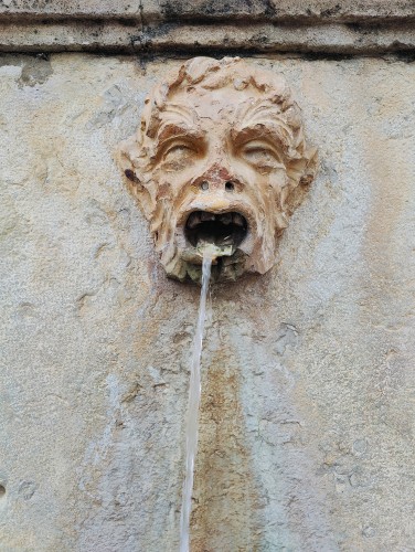 Grumpy stone face with water flowing out of its mouth.