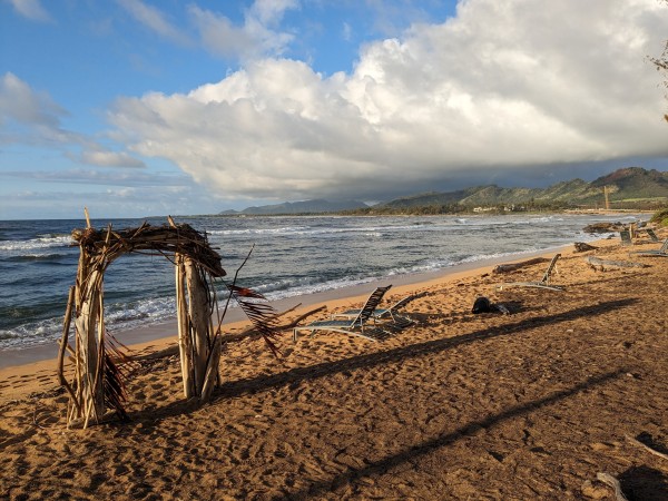 Hawaiian beach stretching into the distance with a wood and palm frond gateway thing built on the beach.
