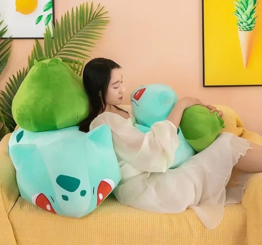 A young lady cuddles up with two Bulbasaur plushes on a yellow sofa