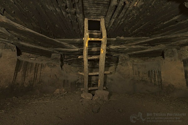 A round hole in the ground, large enough for at least twenty people, with a roof made of ancient fire and smoke scared logs. A ladder made of logs ascends from the center of the structure through a rectangular hole in the roof.