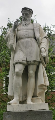 Une statue de monsieur avec une grosse belle barbe et d'élégants collants qui regarde une plante de près 