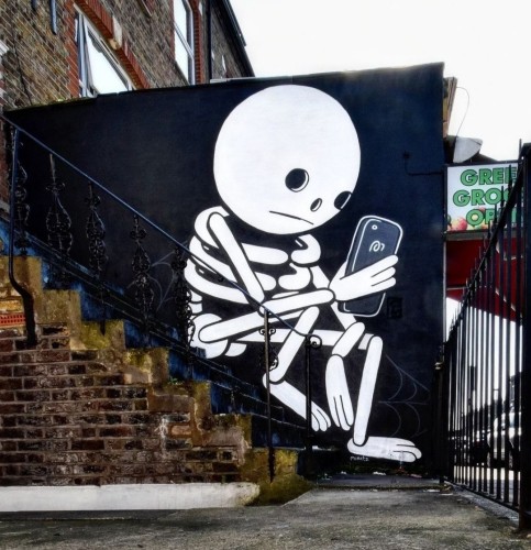 Streetartwall. This cool mural of a skeleton looking at its phone was sprayed/painted on a small slanted exterior wall next to a brick staircase. The simply designed mural shows the skeleton figure sitting, adapted to the staircase in front of it; the background is black, the skeleton white. It has a round head reminiscent of a bowling ball. He is pausing in front of the house, holding a telephone in one hand and looking at it.
Info: The Brazilian artist "Muretz" prefers a black and white color palette, simple but effective strokes and rounded lines to depict figures in various everyday scenes and thus also convey their emotional state