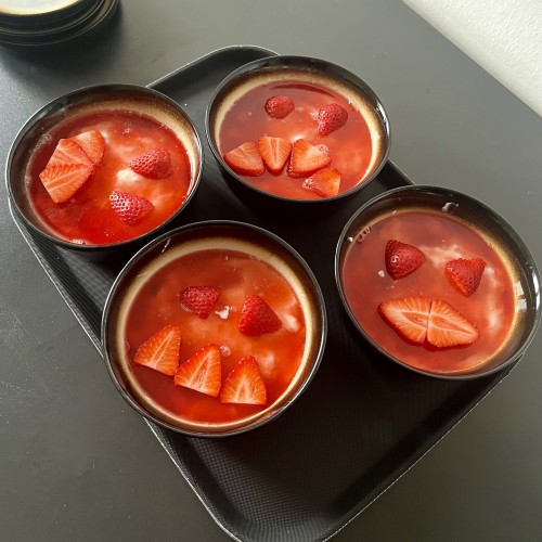 Four bowls of cheesecake with strawberry topping, and some strawberry slices arranged  in face-like patterns.