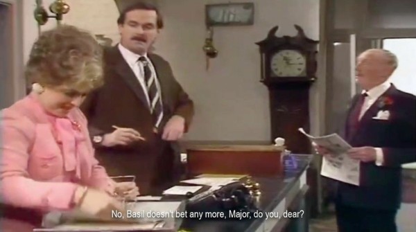 A man and woman standing behind a hotel desk, talking to a guest. “No, Basil doesn't bet any more, Major, do you, dear?”