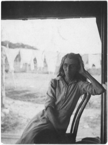  The image is a black and white photograph depicting a woman sitting in front of a window. She appears to be looking out, perhaps observing the surroundings or lost in thought. Her attire suggests a rural setting, possibly indicating that she is living in a remote area. The building behind her has a simple structure with visible wooden elements and a corrugated metal roof.

The background reveals a serene landscape of hills and trees under a clear sky, which contrasts with the stark simplicity of the building. There are no other people visible in the immediate vicinity, adding to the sense of solitude conveyed by the image.

The watermark indicates that this photograph is part of a collection at the Library of Congress, specifically within their Prints and Photographs Division. The text "Mountain woman in the hills near Austin, Texas" suggests that this photo captures the life of a female resident in an area close to Austin, Texas, possibly living among the hilly terrain.

The photograph has a vintage appearance due to its monochrome nature and the style of clothing worn by the woman, which may suggest it was taken several decades ago. The image evokes a sense of timelessness and a glimpse into a simpler time or place.
