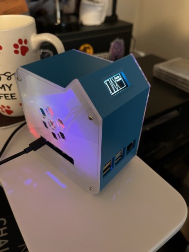 A small, blue, illuminated custom computer case with multiple USB ports, placed on a white surface next to a coffee mug with a paw print design.