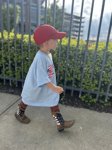 Three year old wearing a Phillies hat and tee, along with cowboy boots. 