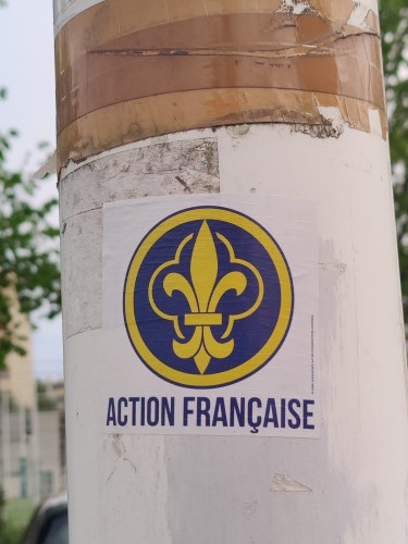 Un sticker Action française sur un poteau blanc.