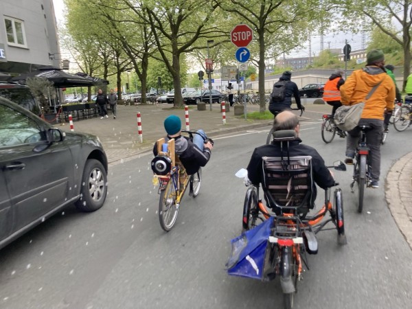 Straße in Hannover. Man sieht das Ende einer Kolonne Radfahrer, teils mit Liegerädern etc. Ein Liegerad hat einen Apparat am Heck, der kleine farblose Seifenblasen auswirft. 