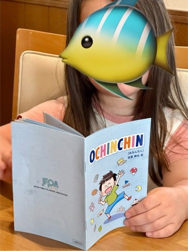 my daughter (face obscured by a fish emoji) reading a booklet from the city hall about looking after penises on babies/small children 