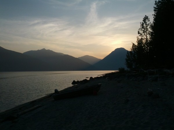 Sunset at a beach of a lake surrounded by mountains.