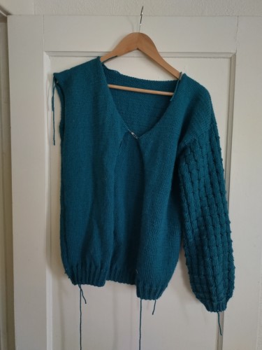 A deep teal hand knit sweater with a simple stockingette body and textured sleeves