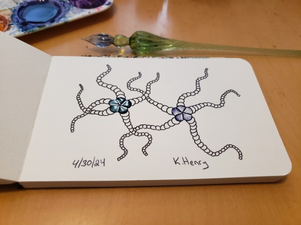 Hand drawn generative art in ink on an open page of my sketchbook. The abstract pattern looks like two starfish dancing with joy, with their limbs intertwined.

My glass dipping pen, and ink pallet are next to my sketchbook.