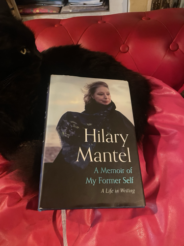 Hilary Mantel’s book ‘A memoir of my former self’, resting on a fluffy black cat on a red sofa