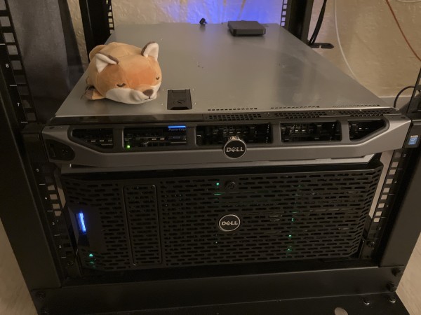 a tiny blob shaped fox plushie dozing on top of two servers in a rack 