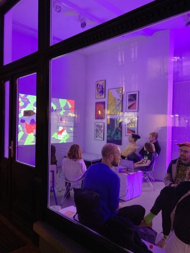 View into the gallery from outside. People inside are playing a videogame that is projected on the wall. 