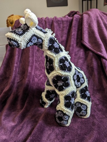 A handmade stuffed giraffe, made of polygonal flower motifs and chenille yarn in black, gray, and white. It's just the right size for a hug. 