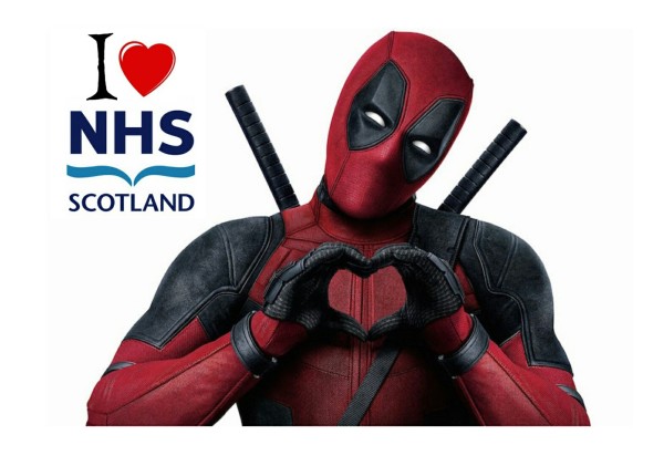 The character Deadpool making a love heart with his hands standing in front of a sign which reads 'I love NHS Scotland ' 