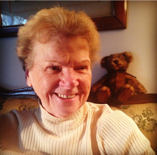 My mom, Betty-Jeanne smiles brightly with bright red hair and a teddy bear over her shoulder. 