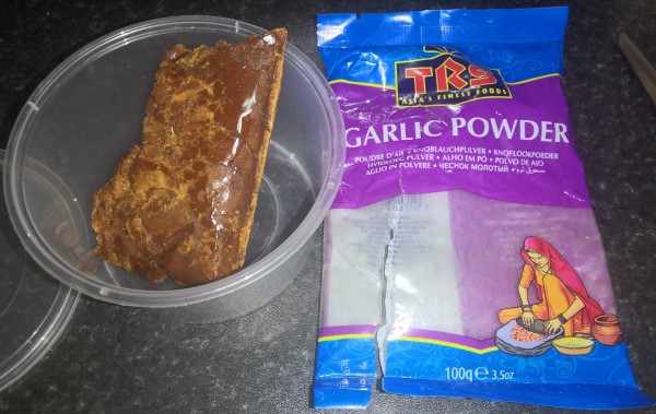 Plastic cup with a solid dark brown mass retaining the shape of the packet in which it was stored. The cut open packet lies beside it. Packet labelled: TRS Asia's Finest Foods
Garlic Powder 100g 