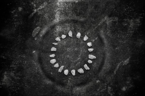 Black and white image of a circle of light coloured stones, on a dark, textured background.