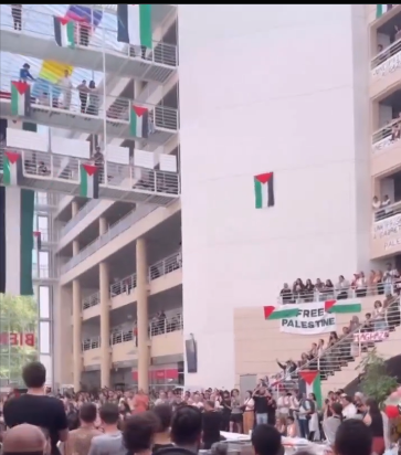 Palestinian flags hanging from several walkways and balconies, with a huge crowd standing at ground level