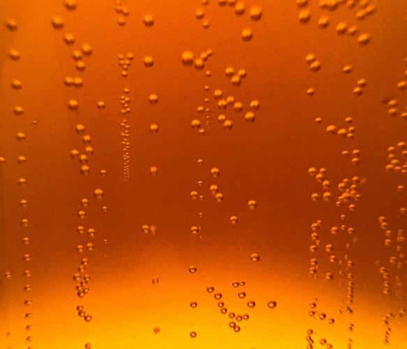 A close-up picture of bubbles rising from the bottom of a glass of Hefeweizen lit from behind. The picture is orange turning to yellow at the bottom.