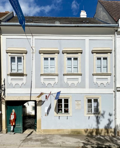 Das Haydn-Haus in Eisenstadt. Wohnhaus aus der Barockzeit, Vorderansicht mit Tortür und zwei Fenstern im Erdgeschoss und vier Fenstern im ersten Stock, blassblauer Anstrich mit weißen Fassendenverzierungen.