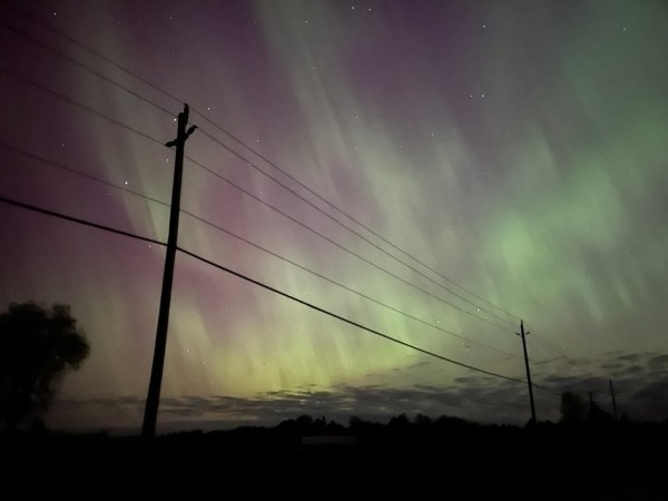 The Aurora borealis fills the sky behind a country road and power lines leading off into the distance.