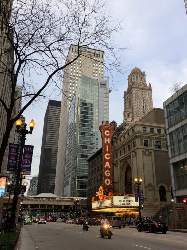 Slightly overcast day on State Street downtown. The Chicago theater is aglow, with its iconic orange-red sign serving as a beacon. 