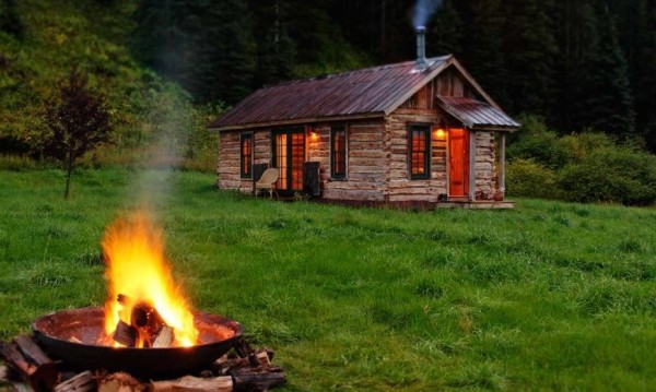 a small cabin in the woods with a fireplace in front of it.
