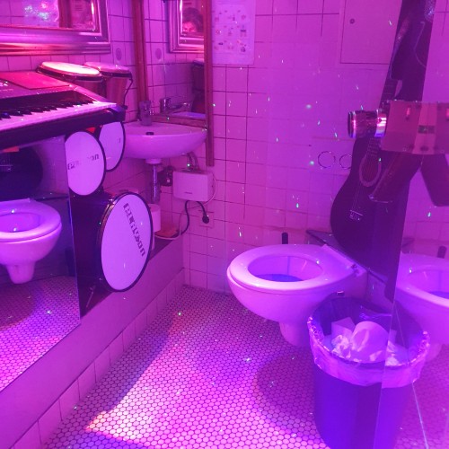 A bathroom (you can see the toilet in front of you), in pink light with disco all dots. It's also full of music instruments. 