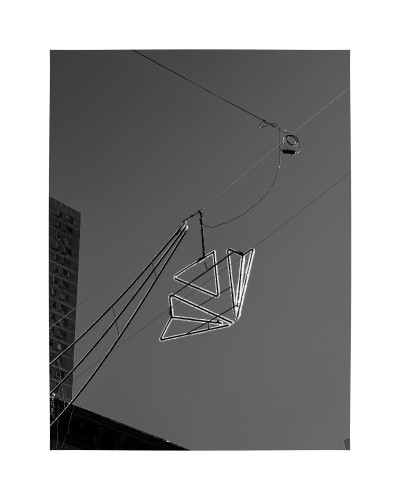 A decorative light made of several triangles strung over a street against a clear sky. 