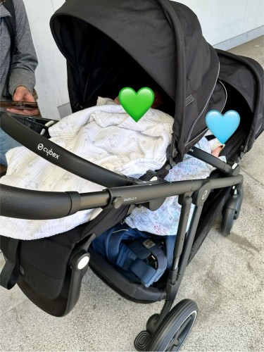 6-week-old twins in a Cybex pram designed for twins, their faces obscured by light blue and green hearts