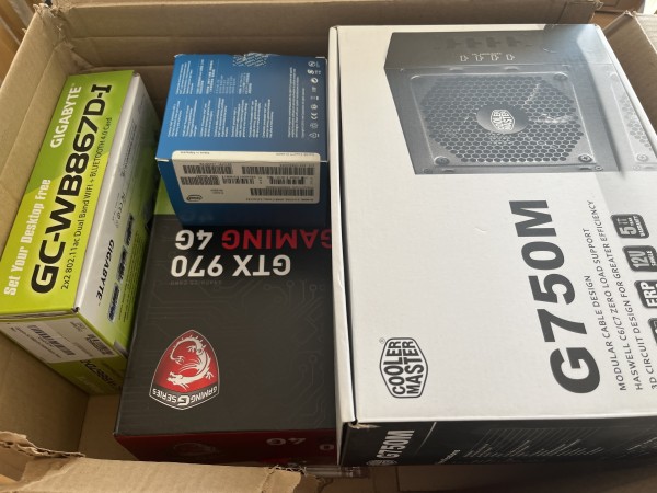 Cardboard box containing various electronics product boxes, including a GIGABYTE GC-WB867D-I Wi-Fi/Bluetooth card, a Sapphire graphics card box, and a Cooler Master G750M power supply unit.