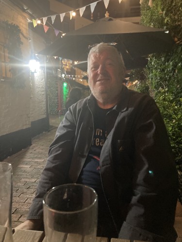 steve looking bemused, sitting at a table outside a pub