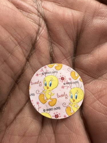 A person's hand holding a small, round object with multiple illustrations of an animated yellow bird character.