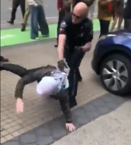 A police officer throws a student protesters violently to the ground.  The student subsequently lands on their face.