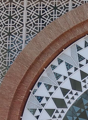 Detail of entrance, Marrakech railway station, Morocco. There are two main regions separated by an arch of thin bricks that runs from the bottom left to the top right. In the top left, the outlines of equilateral triangles and regular hexagons overlap. In the lower right, white triangles have triangular gaps. Reflections of both patterns can be seen in the gaps.