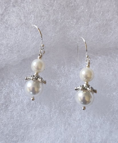 Silver and pearl wire earrings. Two pearls a decorative silver beads, and a tiny round silver bead at the bottom of each. They are on a white backing.