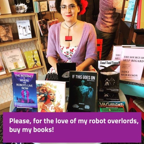 Woman in bookstore at a little table full of books with text please for the love of my robot overlords buy my books 