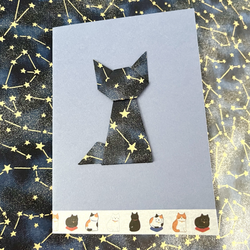 Carte postale représentant un chat en origami en papier étoilé sur fond bleu 