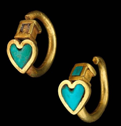 This image features two golden rings, each adorned with a heart-shaped charm. The hearts are outlined in gold and filled with a vibrant turquoise color. At the top of each heart is a small, square-shaped gem that appears to be embedded into the gold. The rings have an aged appearance, indicating possible antiquity.